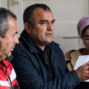 Men and women look at a man holding a notebook as part of a Mahalla Committee self-governance group