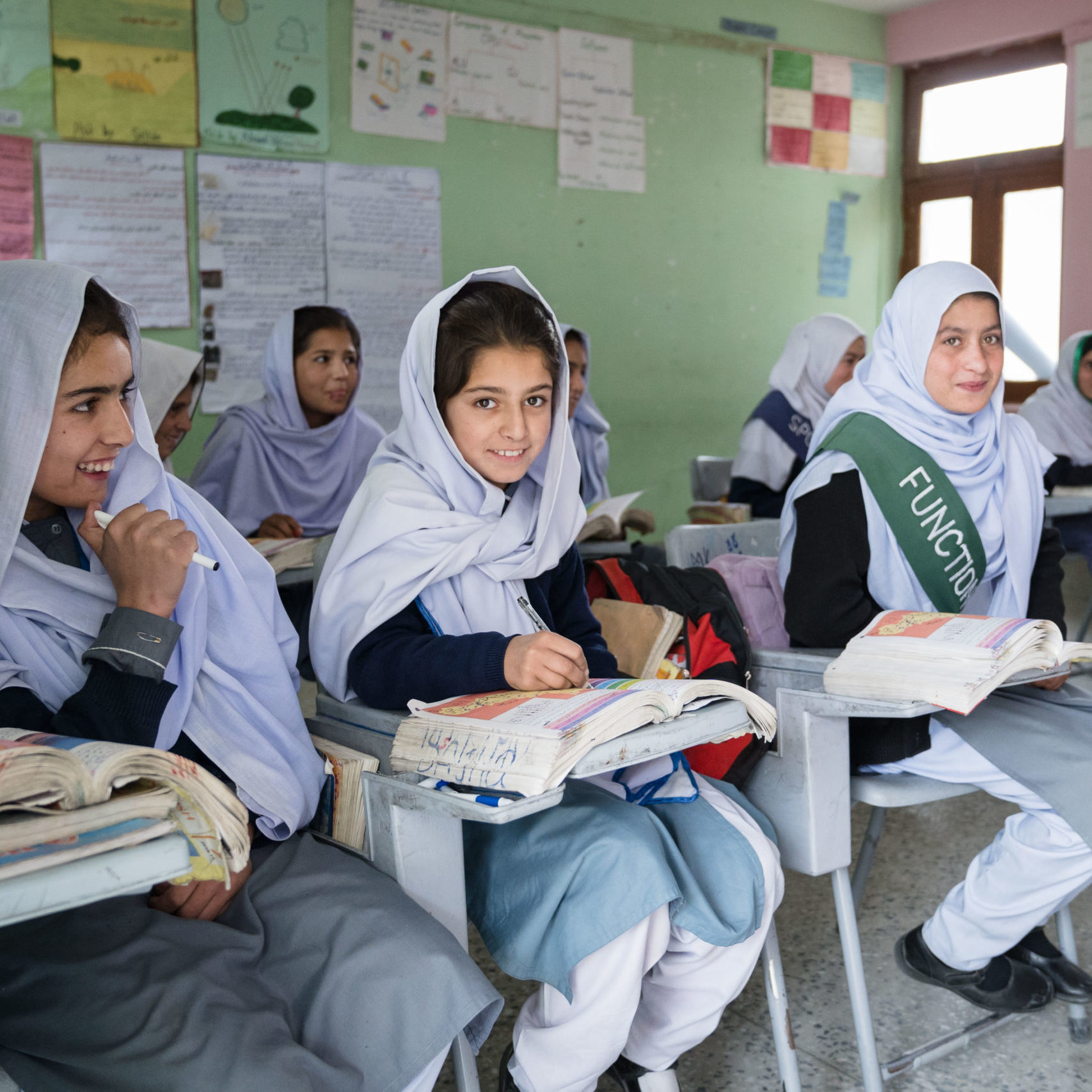 a classroom of young women wearing headscarves with books and posters