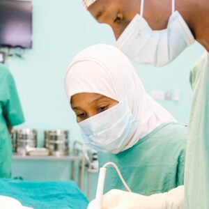 Health and nutrition: three healthworkers wearing green scrubs and wearing facemasks perform a medical procedeure.