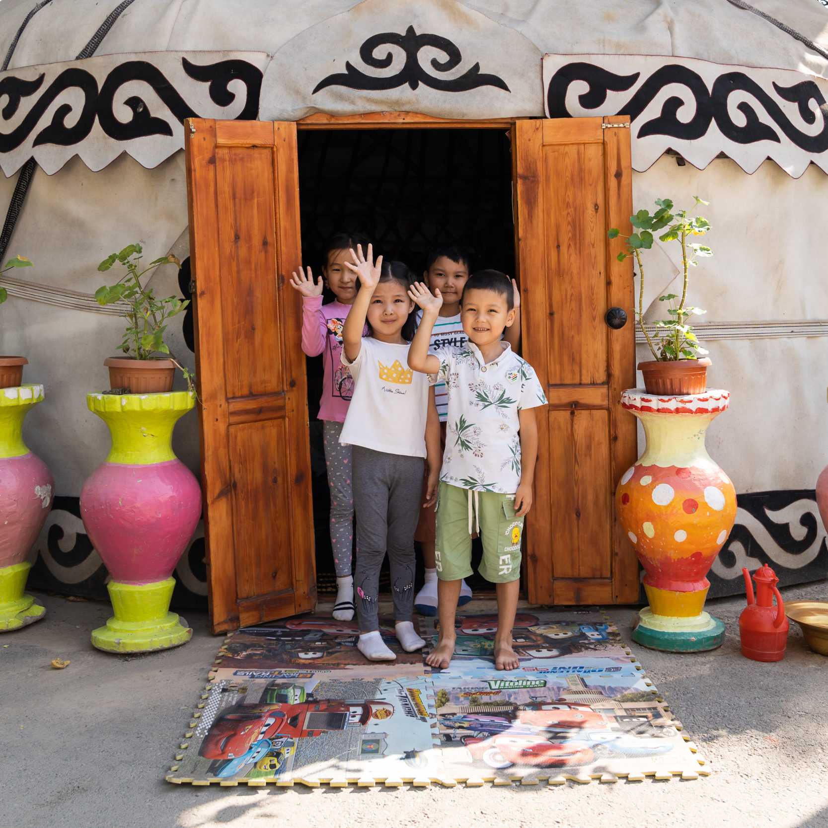 Children wave from the doorway of their traditional-style Kyrgyz classroom building.
