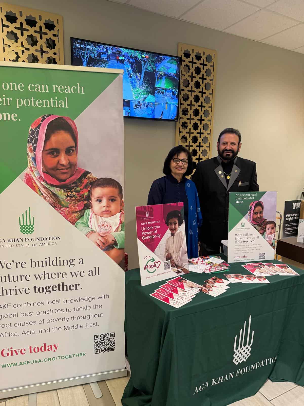 Two volunteers stand behind a table with AKF USA promotional materials.