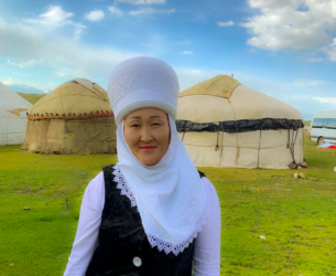 Zuura Ibraimova stands in front of her yurts in traditional dress.