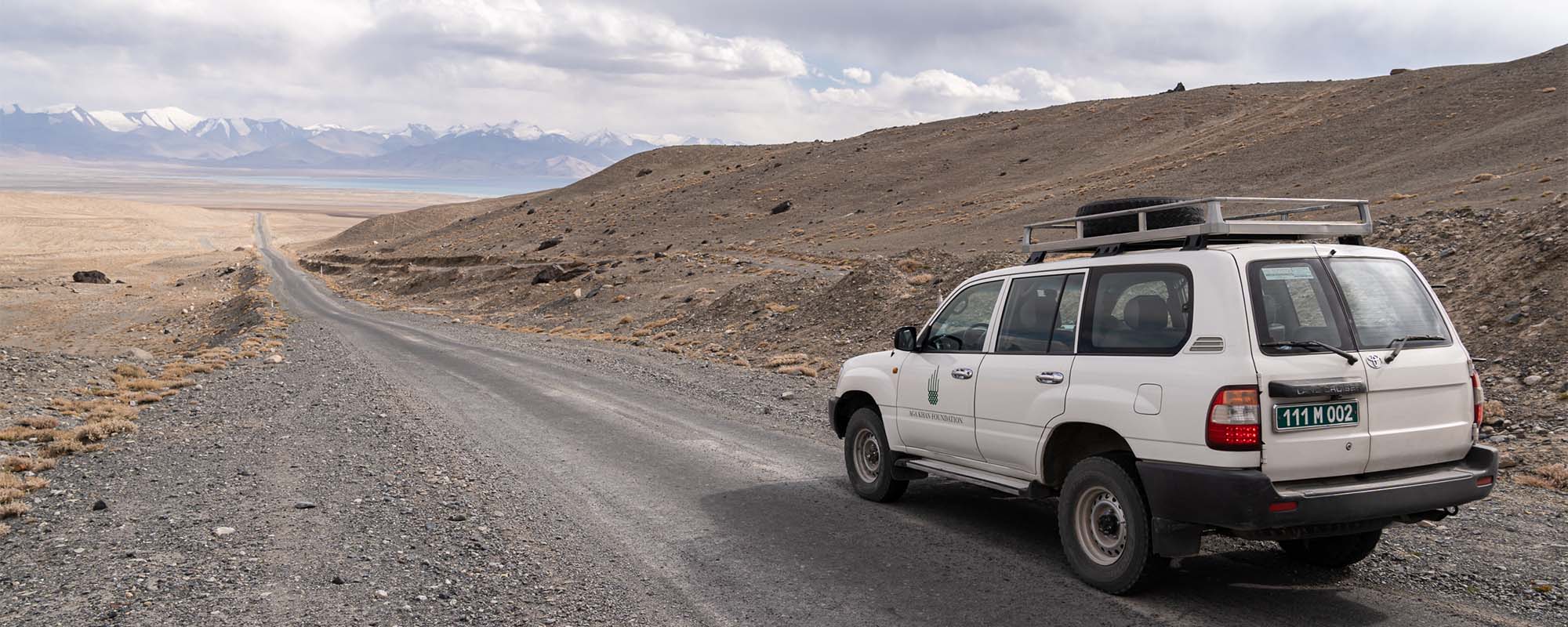 An SUV with the Aga Khan Foundation logo drives on a dirt road in a remote part of Tajikistan.