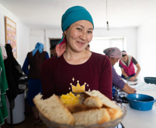 Woman holds out plate of bread as others work in the backgroun