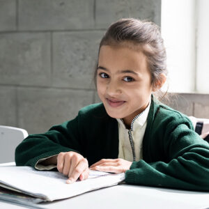 A girl sits at a desk pointing to words in a book on her desk