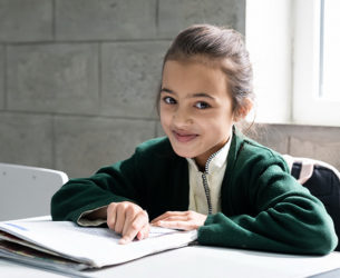 A girl sits at a desk pointing to words in a book on her desk