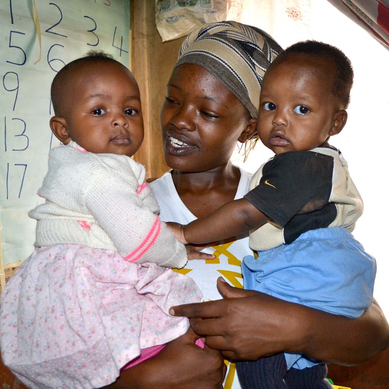 A Kenyan woman holds two babies in a classroom.