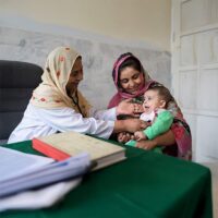 A baby held in his mother's arms is examined by a female doctor.