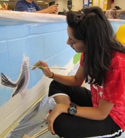 Aga Khan Foundation Dallas Youth Ambassador painting a mural in the Barron Elementary School library. The Youth Ambassador's service project was inspired by the Aga Khan Foundation's Reading for Children project.