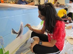 Aga Khan Foundation Dallas Youth Ambassador painting a mural in the Barron Elementary School library. The Youth Ambassador's service project was inspired by the Aga Khan Foundation's Reading for Children project.