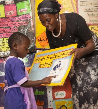 A teacher holds a poster as a student points to a picture on the poster