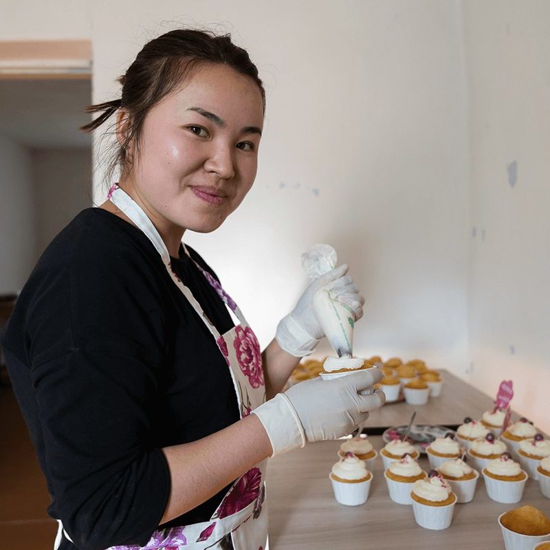 A woman wears gloves while decorating cupcakes