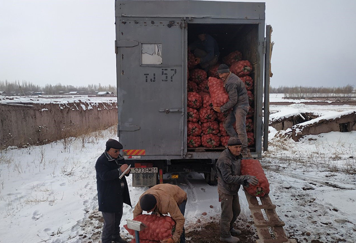 Four men unload sacks of potatoes from a truck. Snow is seen on the ground.