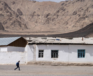 A small child with a backpack is pictured walking in front of buildings and mountains in the background