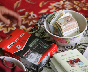 A calculator, bowl of money, and record book are used by the community-based savings group.