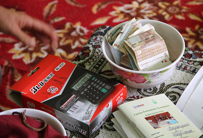 A calculator, bowl of money, and record book are used by the community-based savings group.