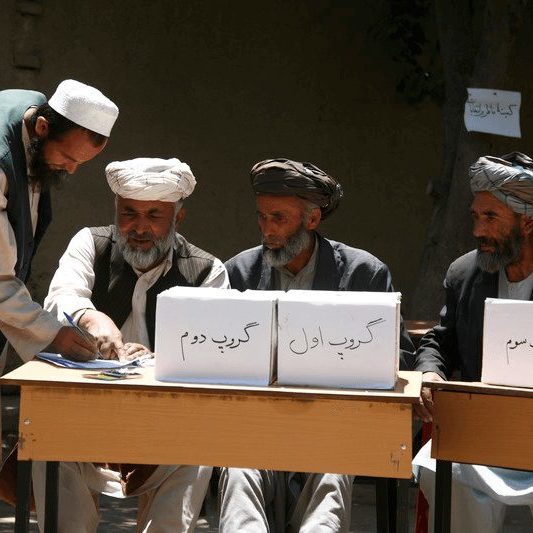 Four men sit behind ballot boxes